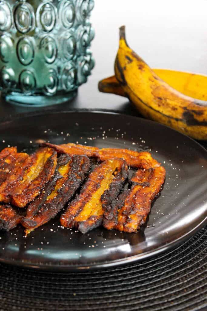 Fried plantains on a black plate with salt.
