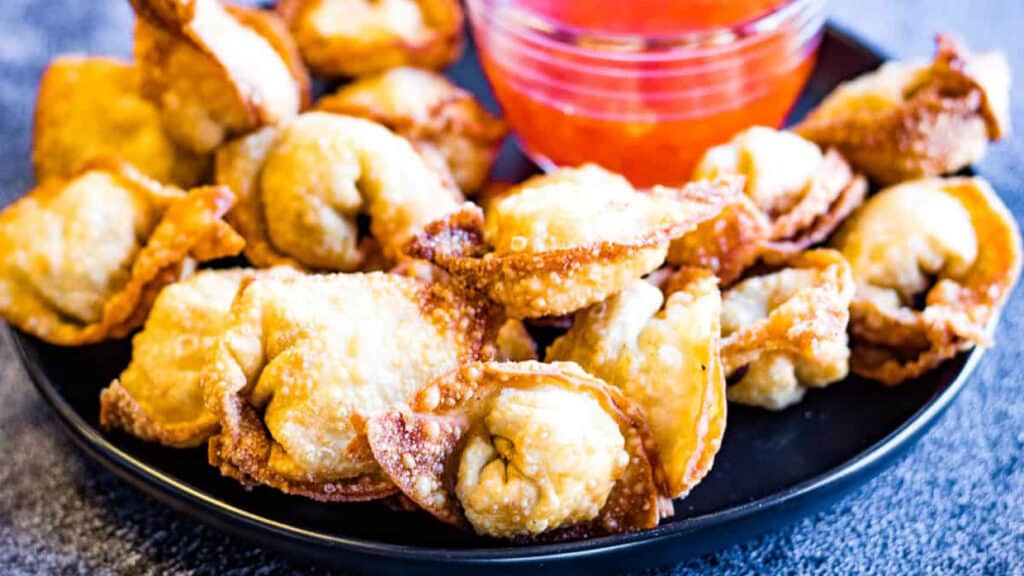 fried wontons on a black platter with dipping sauce.