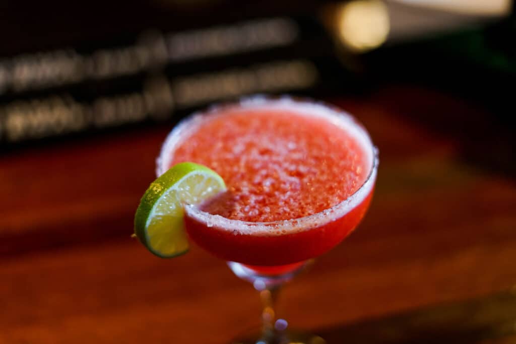 a frozen strawberry margarita with a sugar rim and a lime wedge.