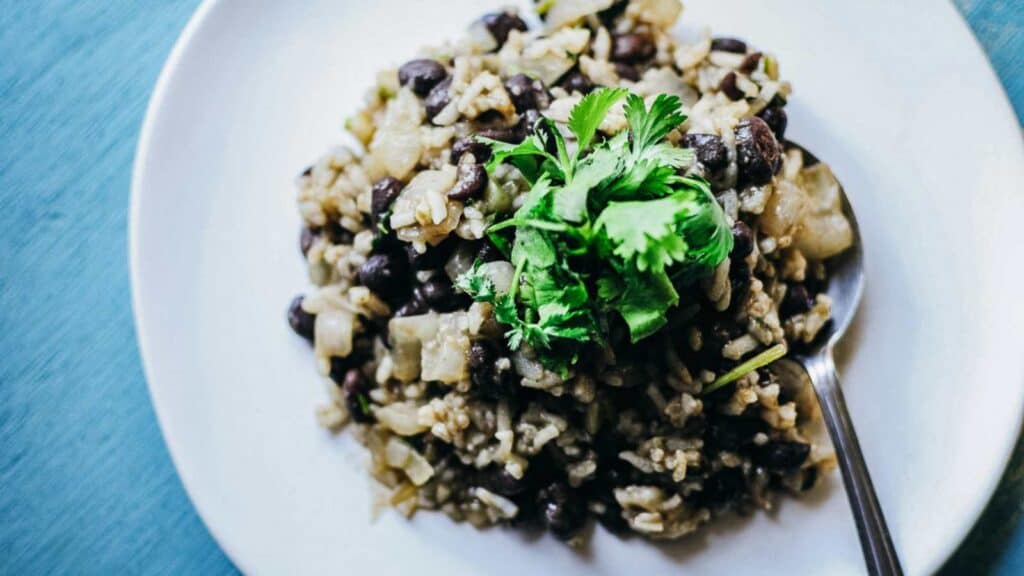 A white plate topped with white rice, black beans and green cilantro.