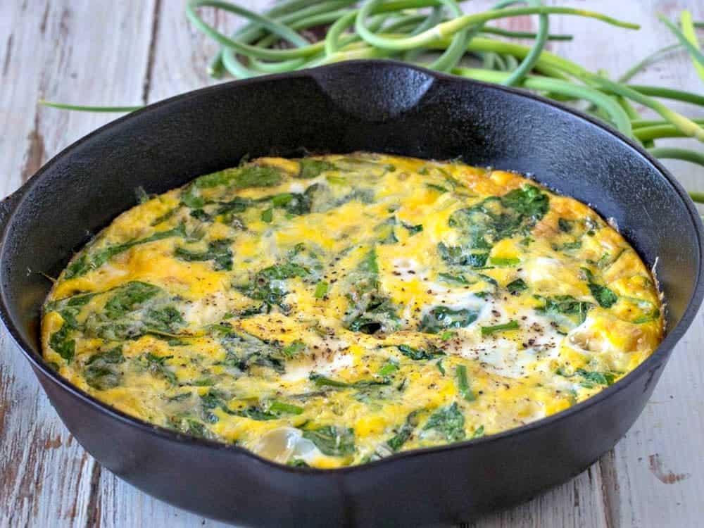Spinach frittata in a cast iron skillet with garlic scapes in the background.