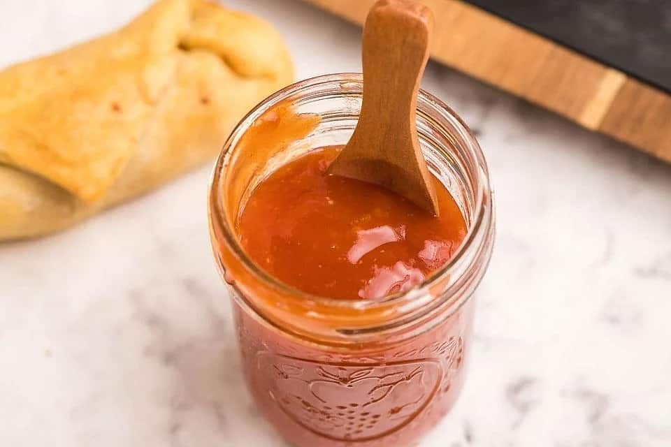 A small jar filled with homemade sweet and sour sauce. 