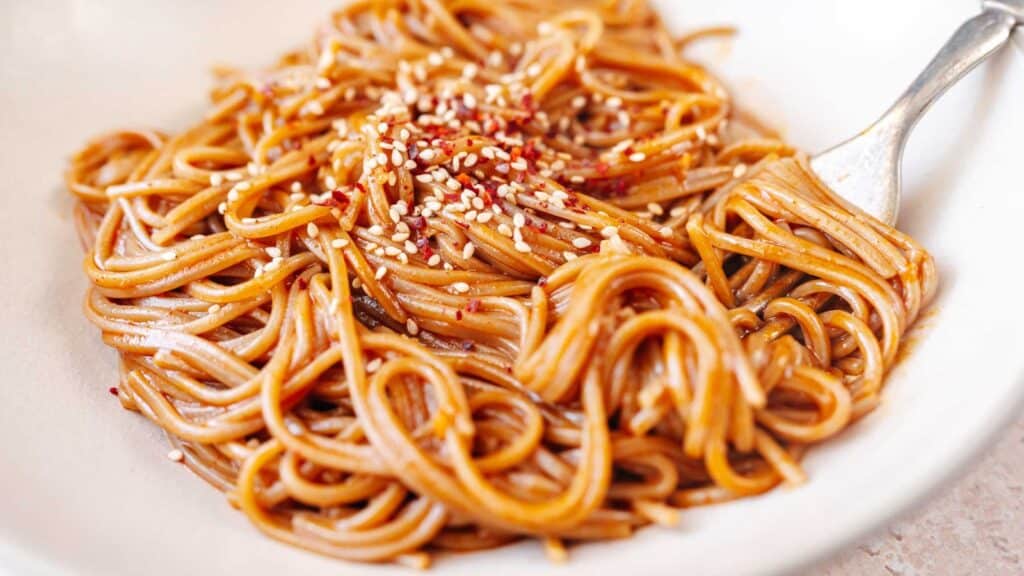 A white bowl filled with noodles coated in a red sauce.