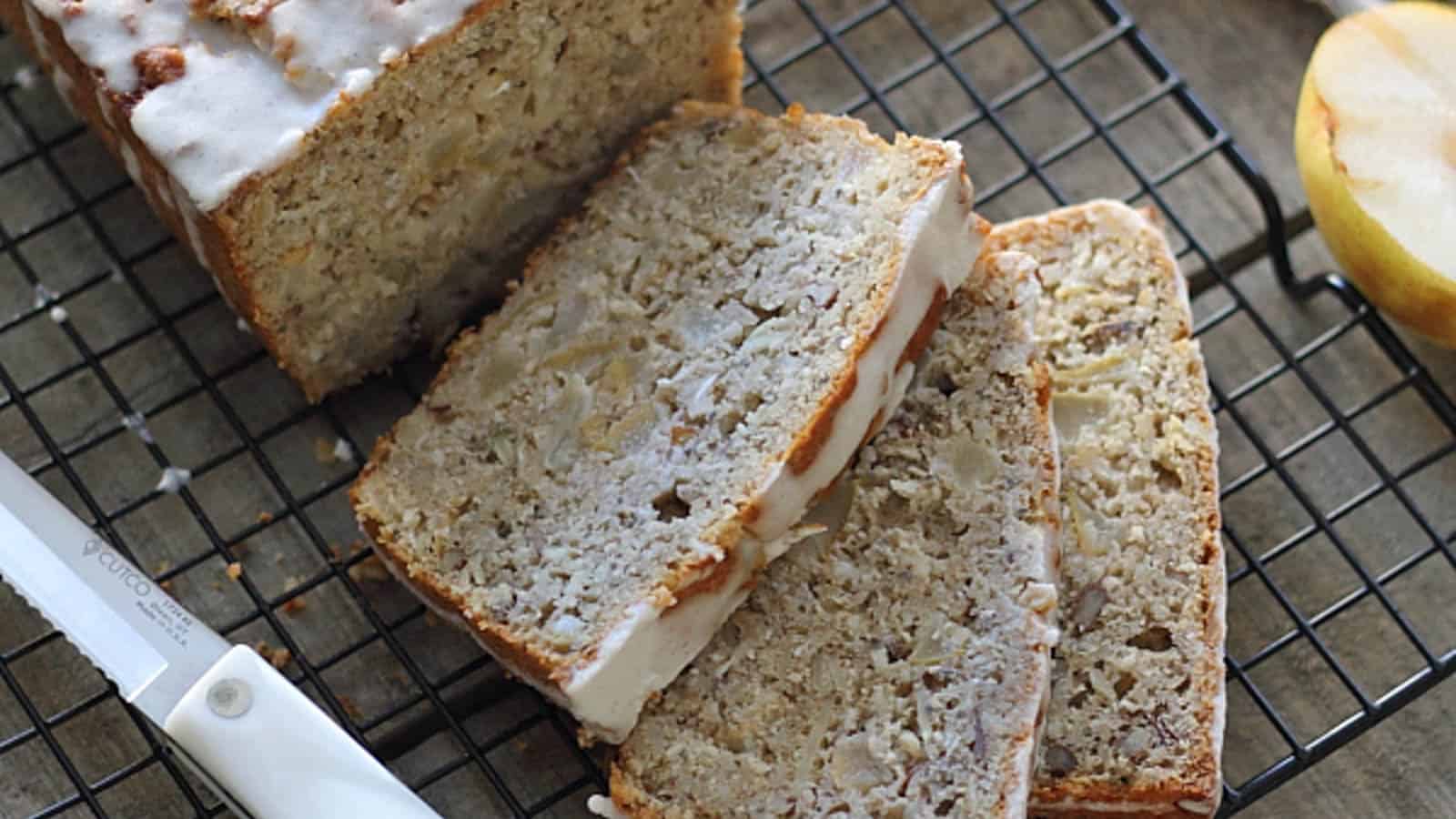 Granola pear bread with icing sliced on a cooling rack.