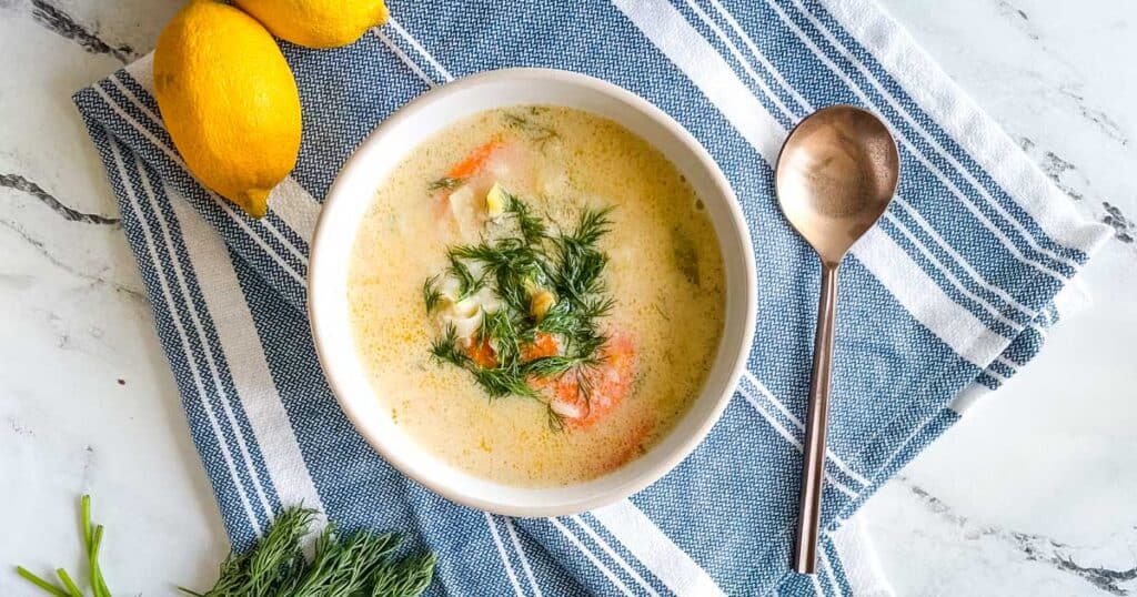 a bowl of greek chickpea soup garnished with dill on a blue and white linen with a gold spoon.