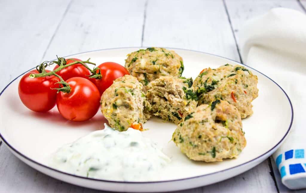 A closeup shot of Greek Meatballs on a round plate with small tomatoes.