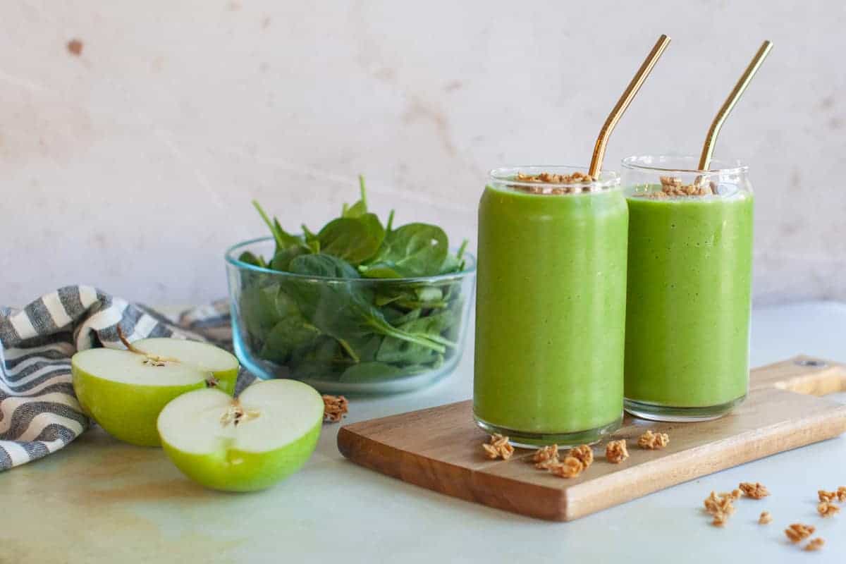 Two green apple smoothies on a wooden board.