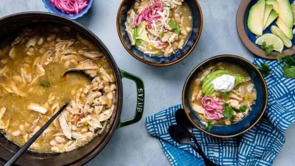 big pot of green chicken chili with smaller bowls on the side.