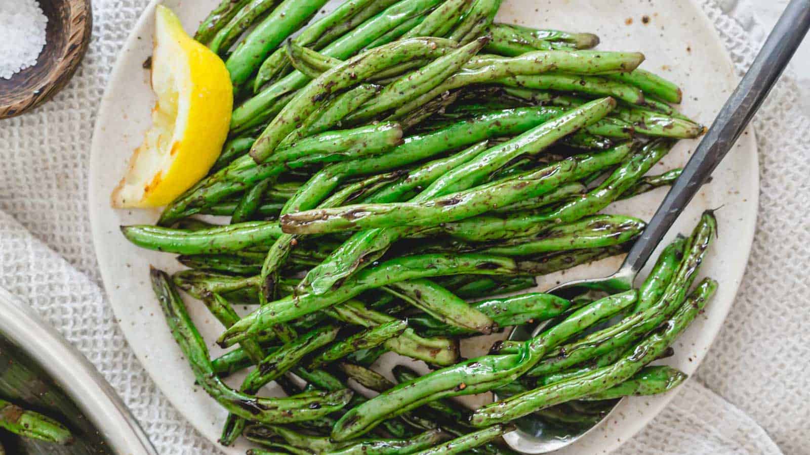 Grilled Asian green beans on a plate with a lemon wedge.