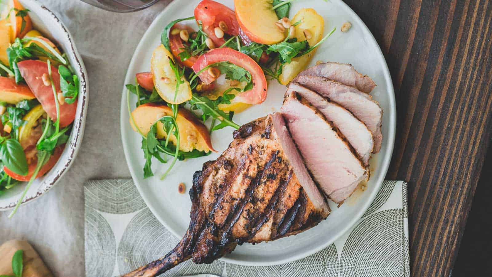 Grilled pork chop on a plate with peach and tomato salad.