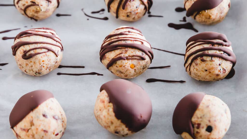 Healthy cookie dough bites drizzled and dipped in chocolate on parchment paper.
