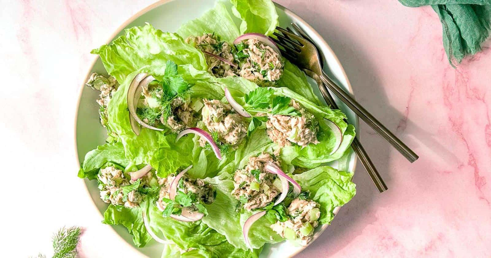 Healthy Tuna salad without mayo sits on a bed of iceberg lettuce surrounded by two forks, dill, and a green linen.