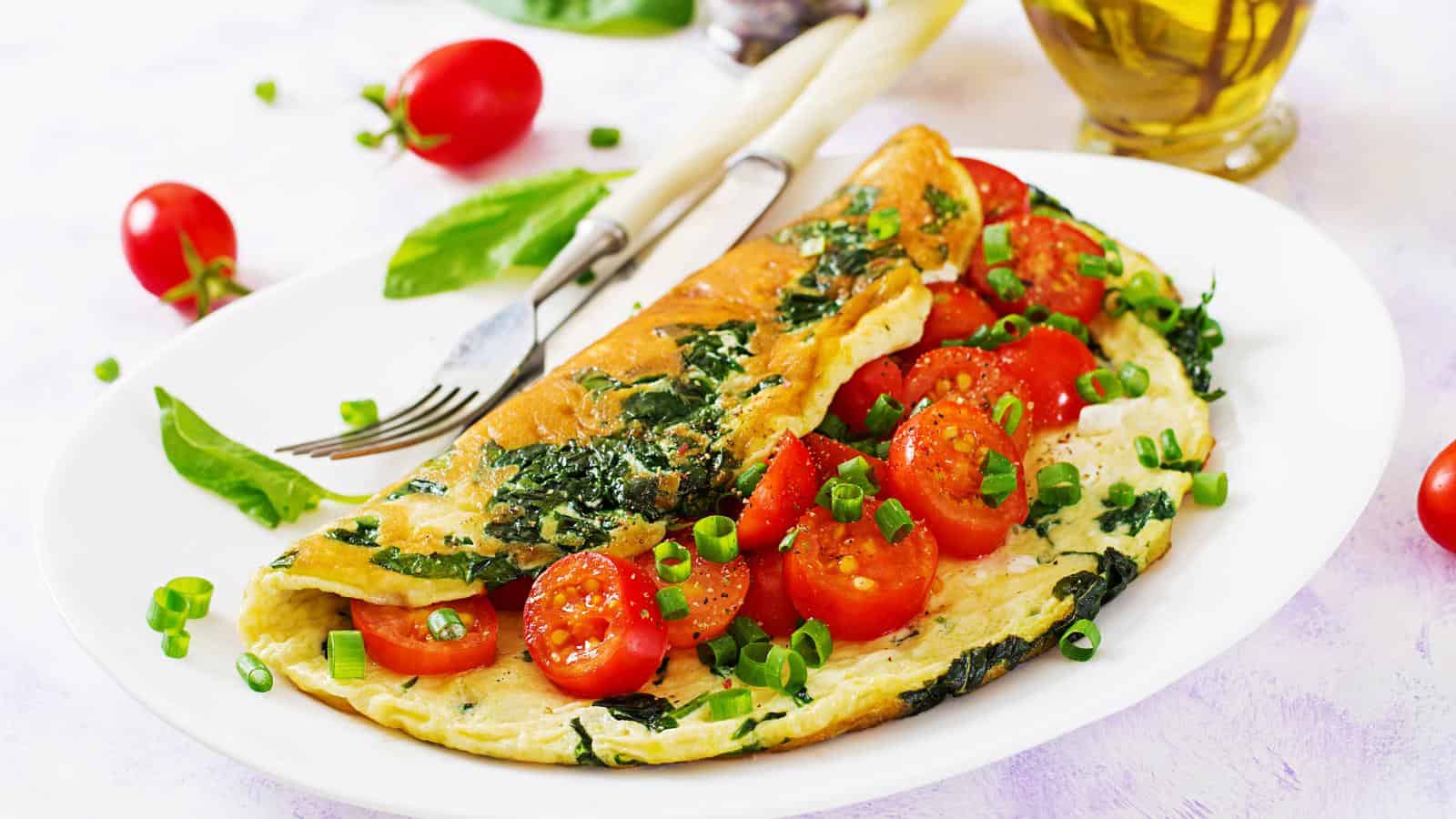 Easy Keto Omelette on white plate with fork and tomatoes.