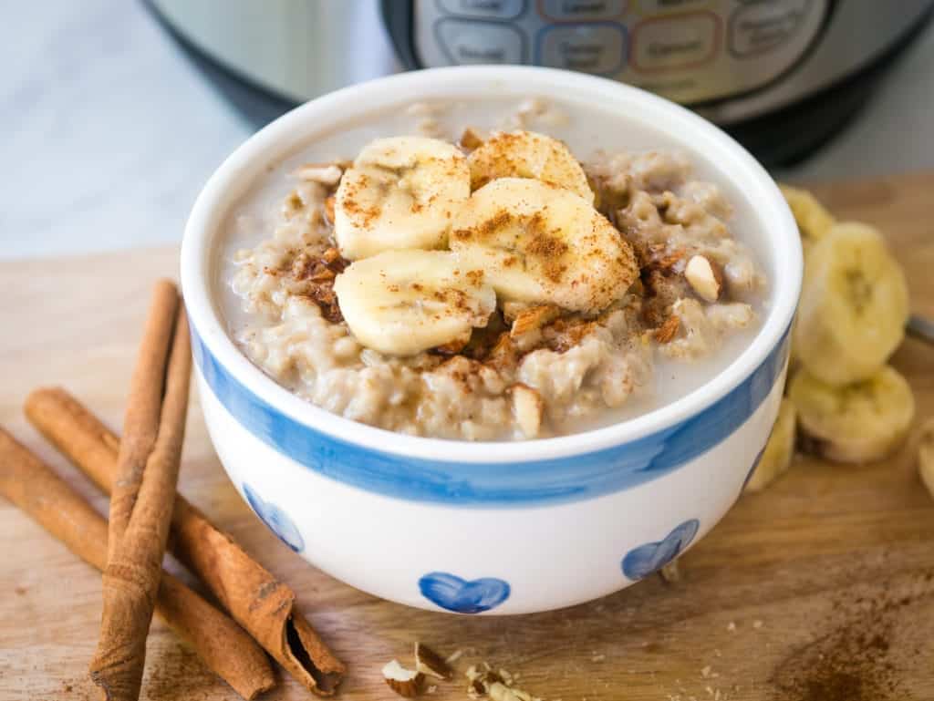 Oatmeal topped with cinnamon and bananas in a blue bowl with cinnamon sticks.