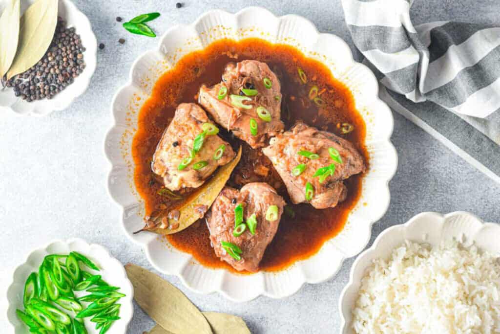 Overhead shot of a plate of chicken adobo with rice and scallions on the side.