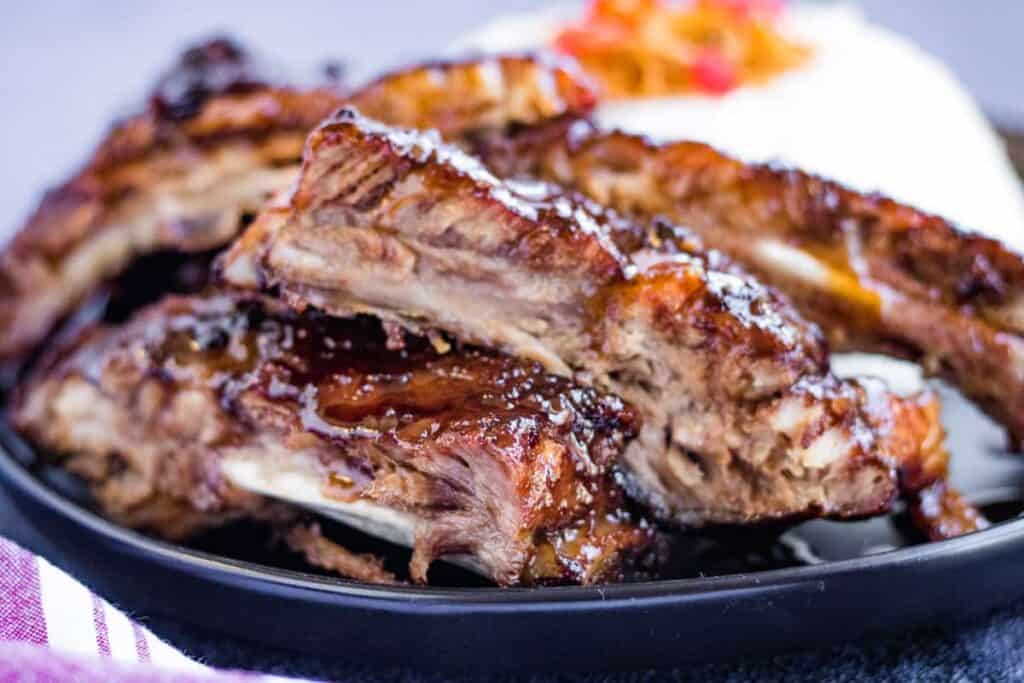 A pile of hoisin glazed spare ribs with rice in the background.