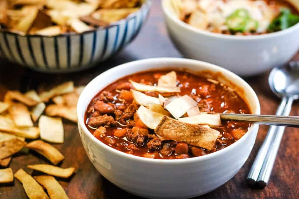 A white bowl with turkey chili and baked tortilla strips.