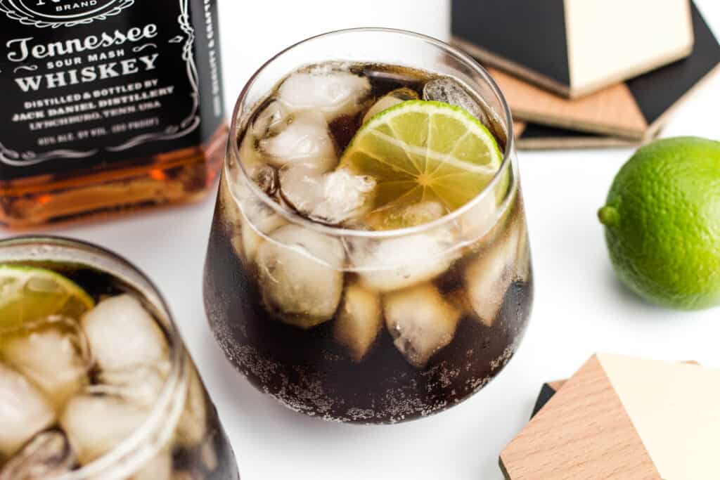 a bottle of Jack Daniel's rests next to two cola cocktails.