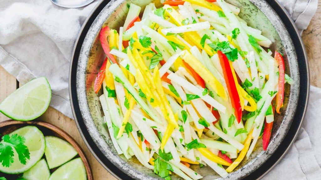 Julienned jicama, mango and pepper salad with a honey lime dressing in a metal bowl.