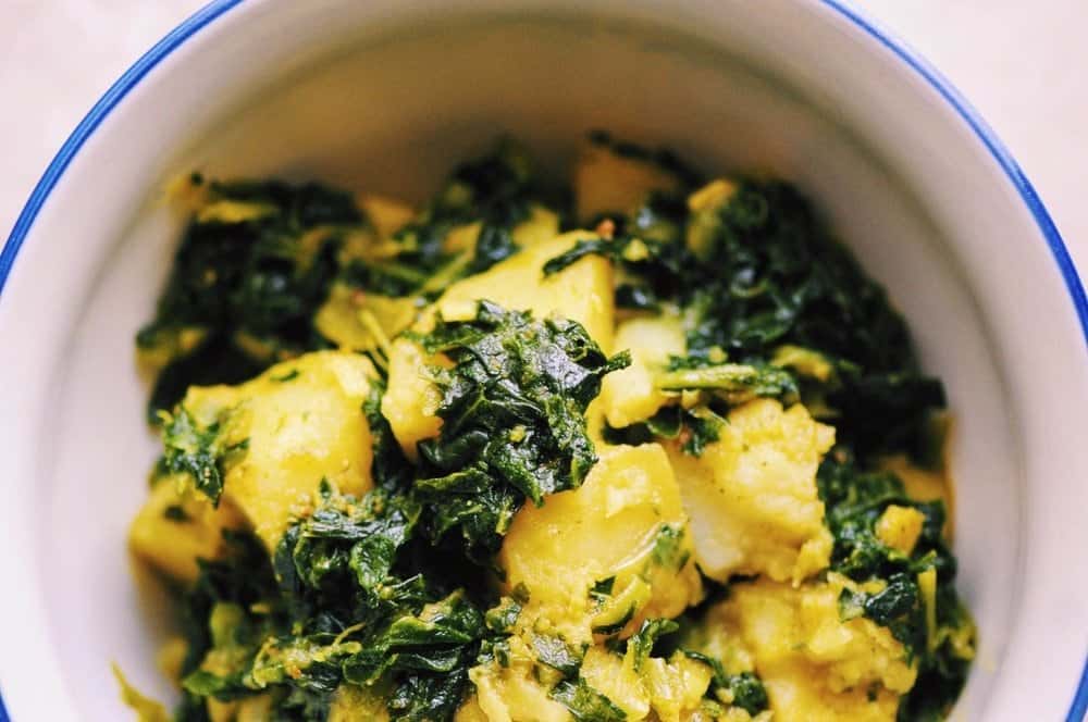 A white bowl filled with cooked greens and yellow potatoes.