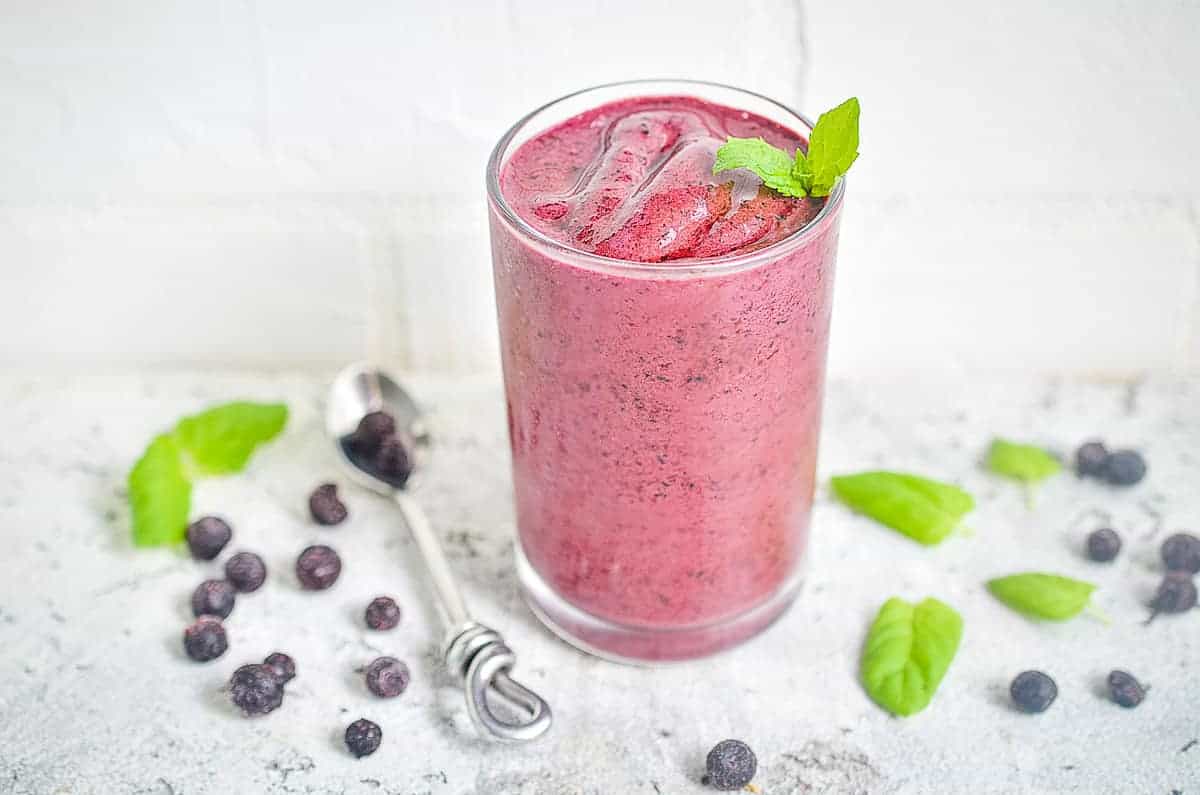 Blueberry smoothie in a glass with mint leaves.