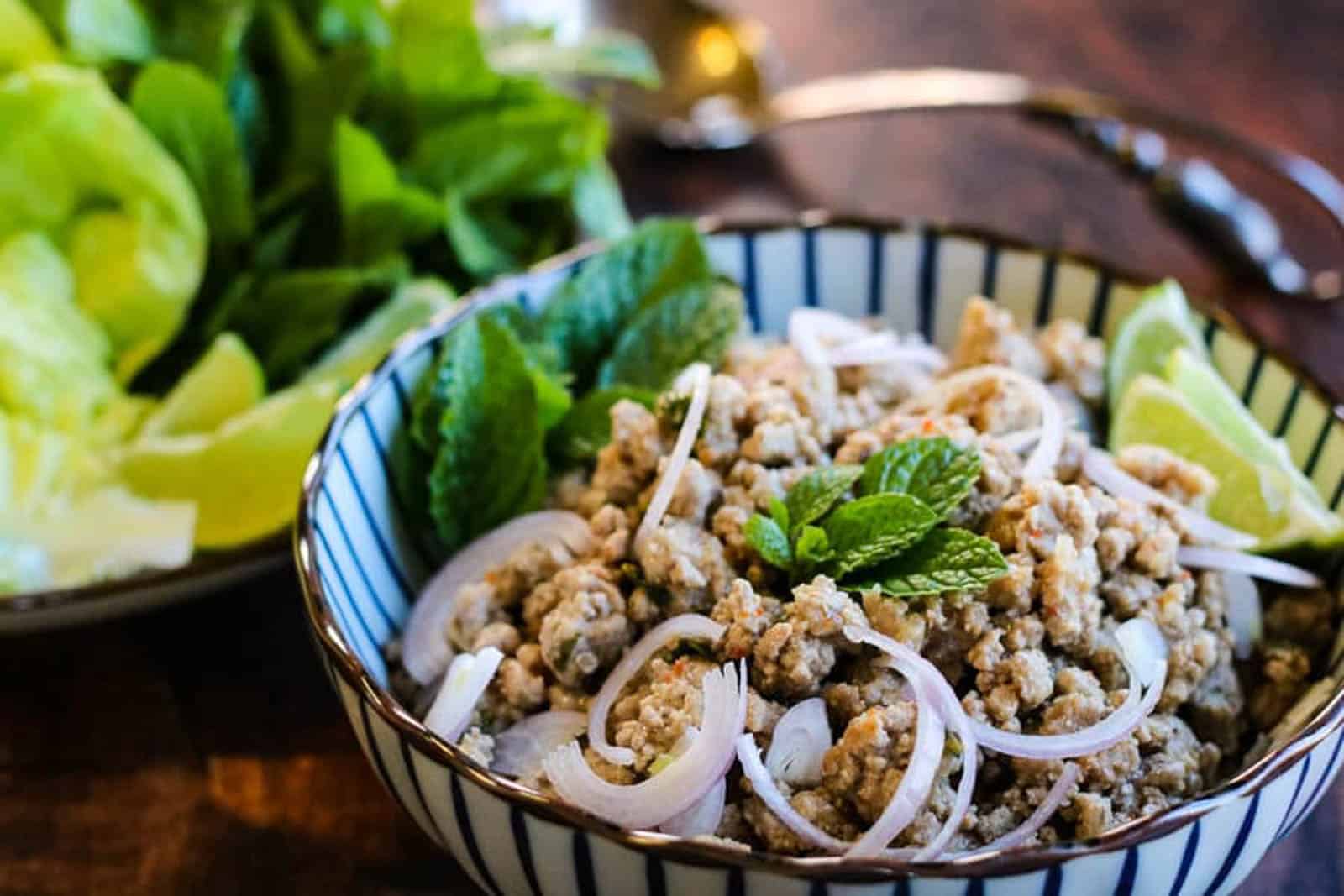 Low angle shot of a striped bowl filled with Thai larb salad garnished with shallot slices.