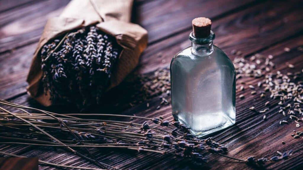 A small glass bottle filled with clear liquid resting next to a bundle of dried lavender.