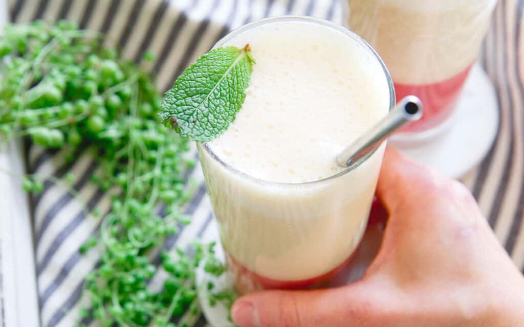 Layered strawberry ginger peach smoothie in a glass with mint leaf garnish.