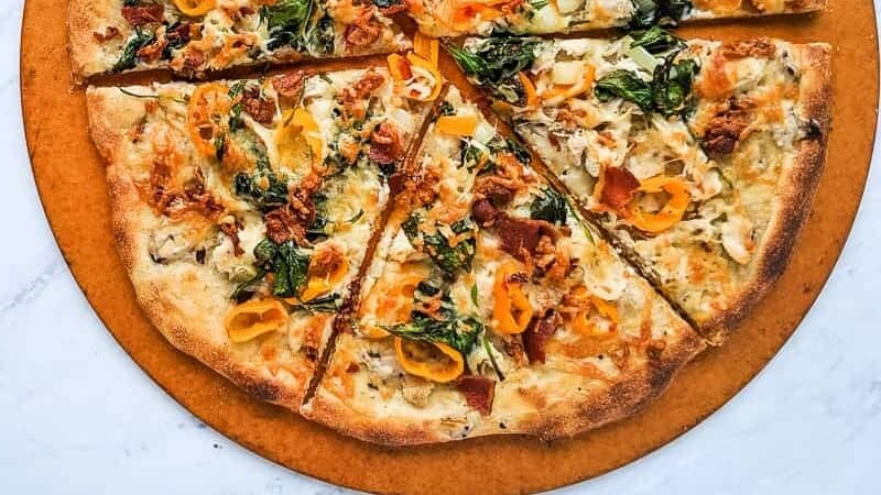 A pizza with spinach and turkey on a wooden board.