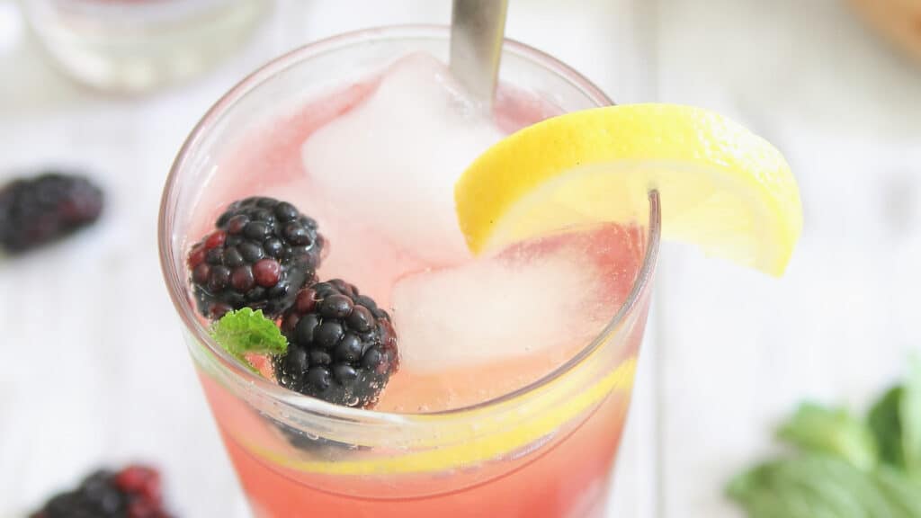 Blackberry lemon mocktail in a tall glass with a stirring spoon.