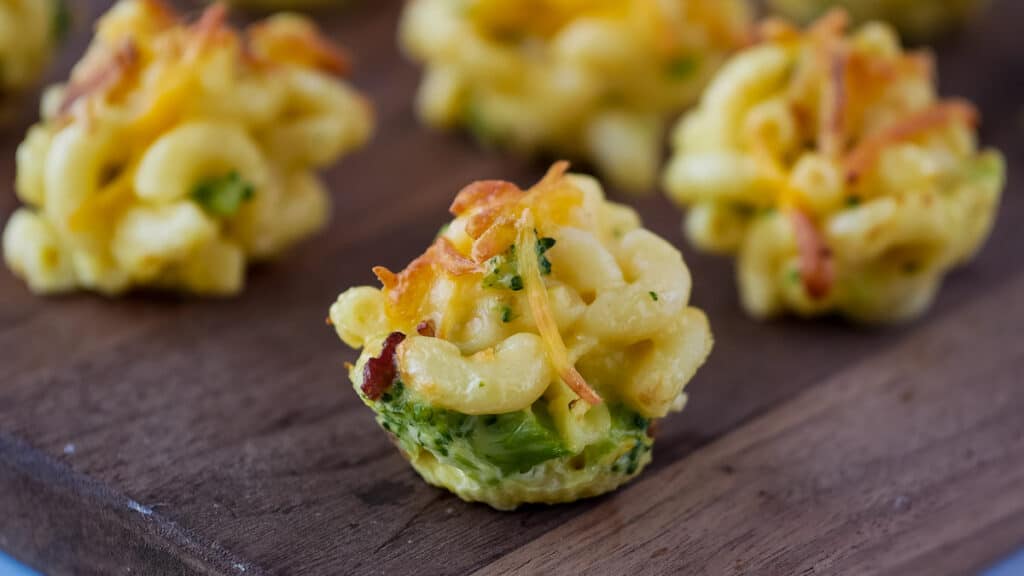 mac and cheese bites with broccoli on a wooden cutting board.