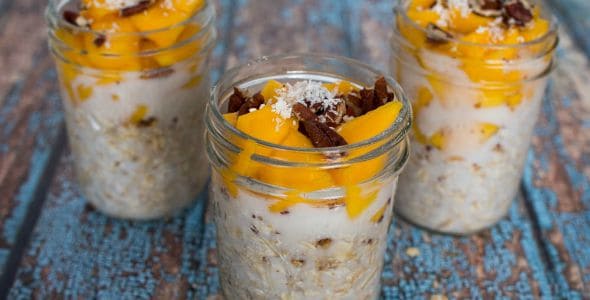 Three jars of overnight oatmeal in mason jars topped with mangos and coconut.