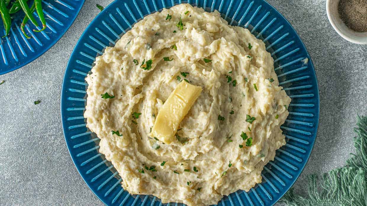 Top view of blue bowl of mashed potatoes with butter and parsley.
