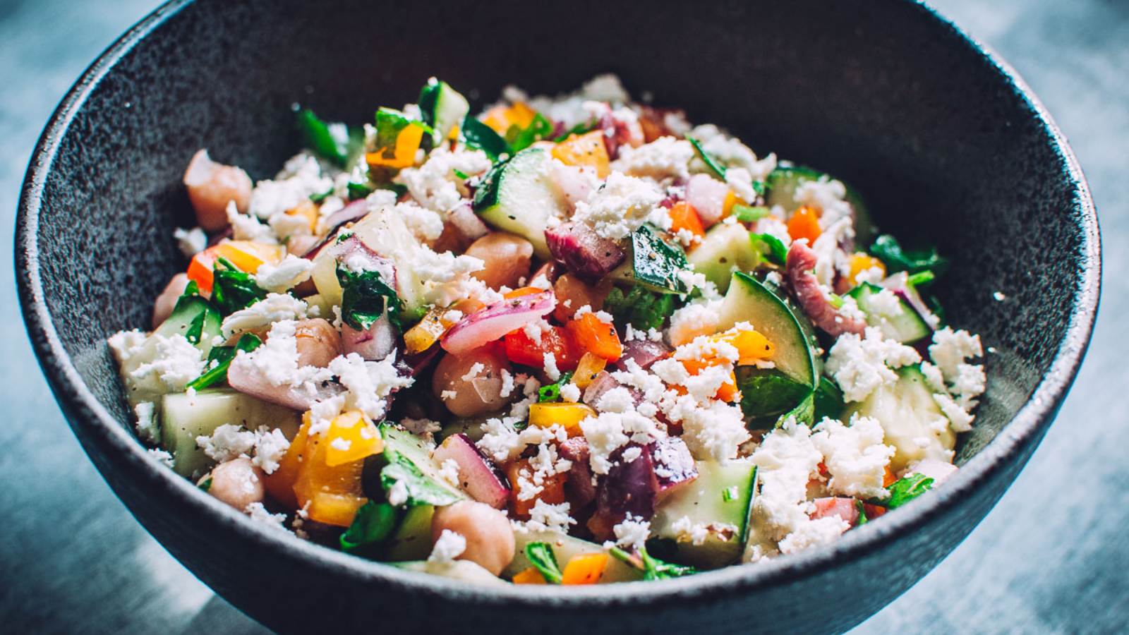 A black ceramic bowl filled with a rainbow medley of salad ingredients.