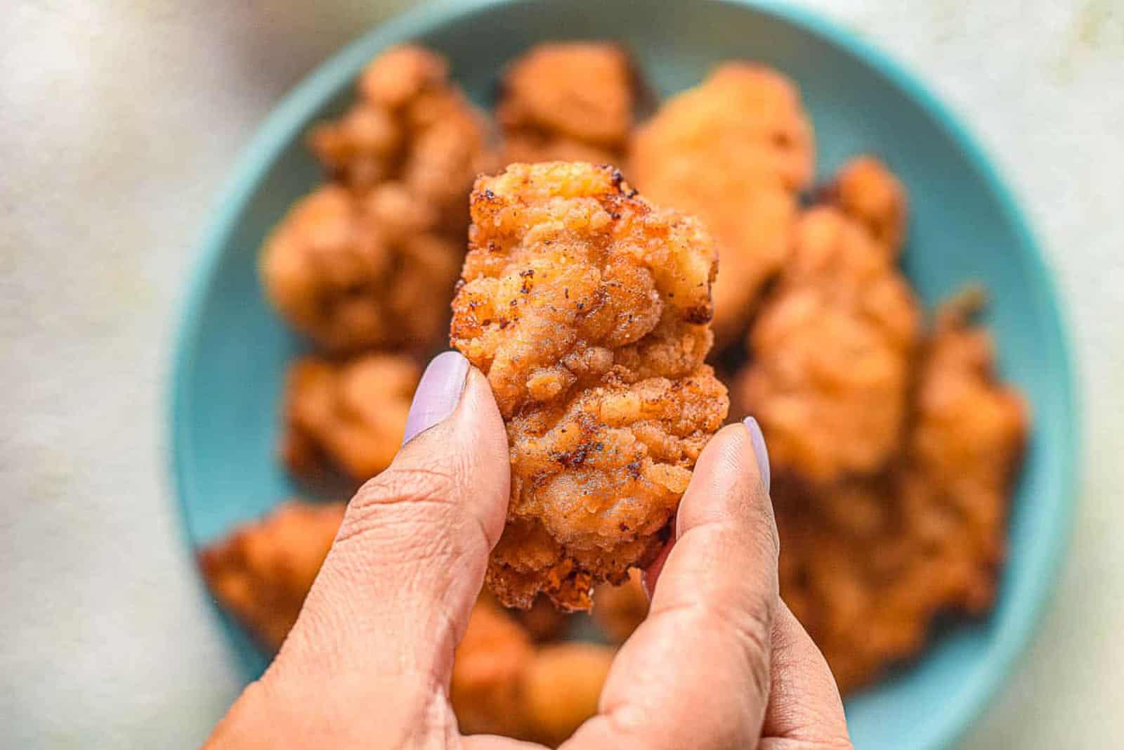 A hand holding a crispy piece of mochiko chicken.