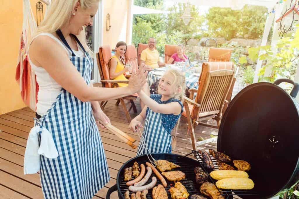 A mother and daughter at the grill with friends in the background.