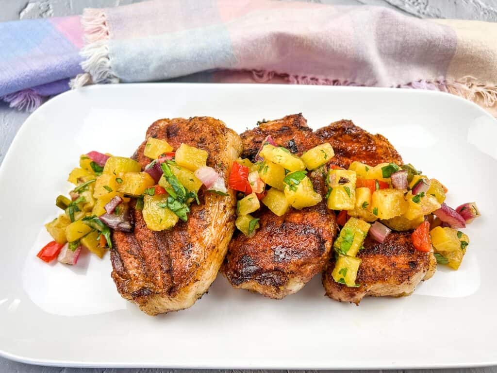 Grilled pork chops on a platter with pineapple salsa.