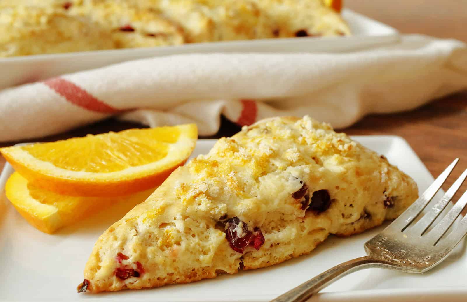 An orange cranberry scones on a white plate with a fork.