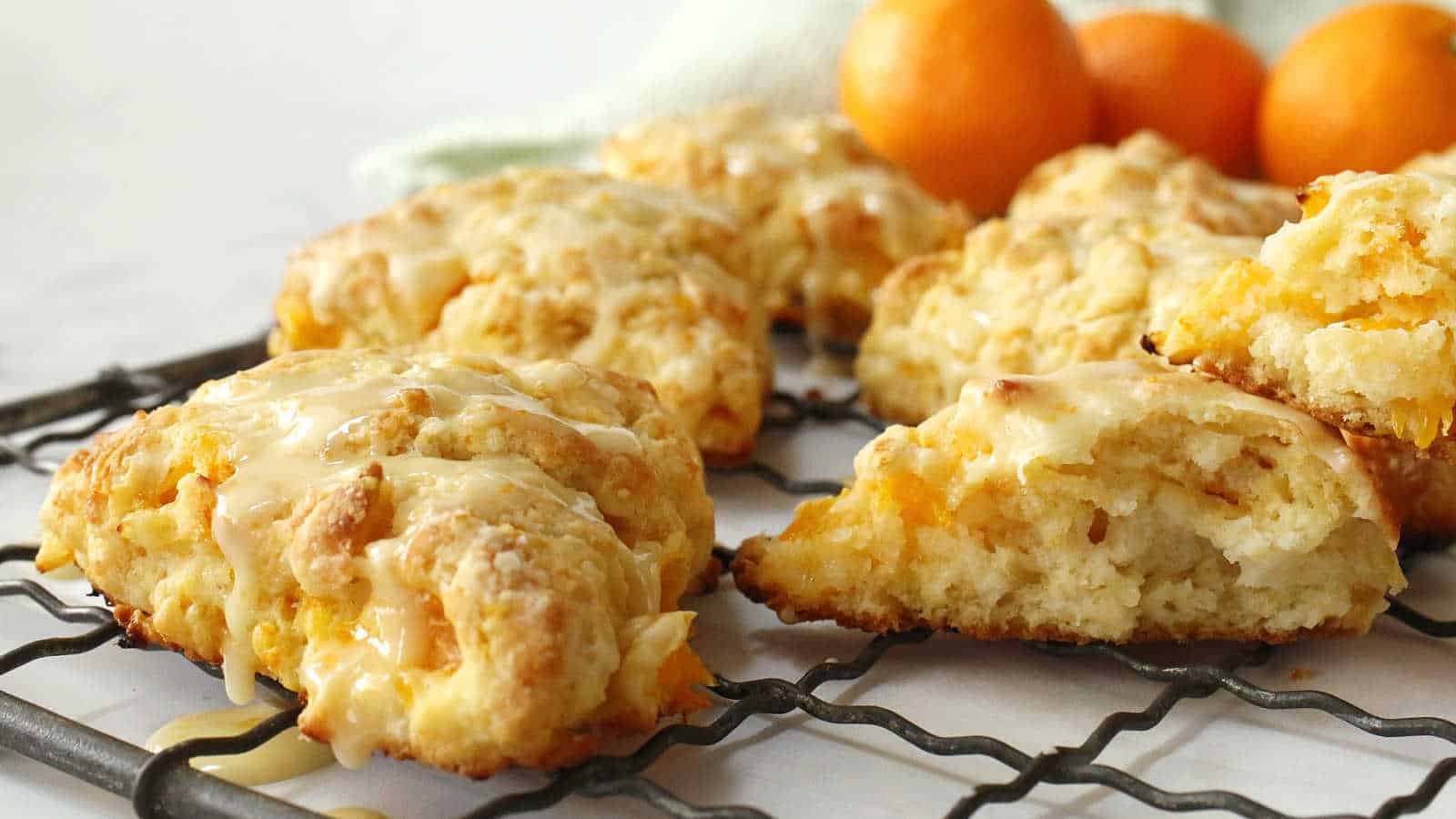 Orange scones on a wire rack with oranges in the background.