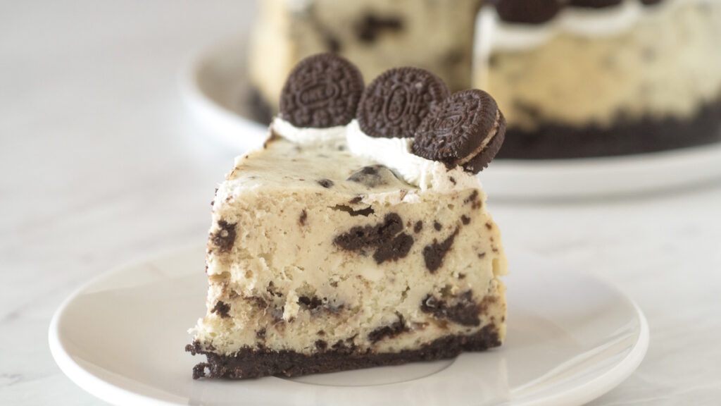 Slice of Oreo cheesecake topped with mini Oreos on a white plate.