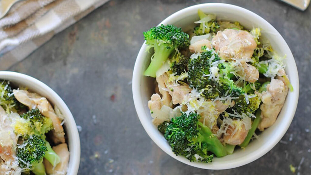 Chicken and broccoli in a small white bowl with parmesan and lemon zest.