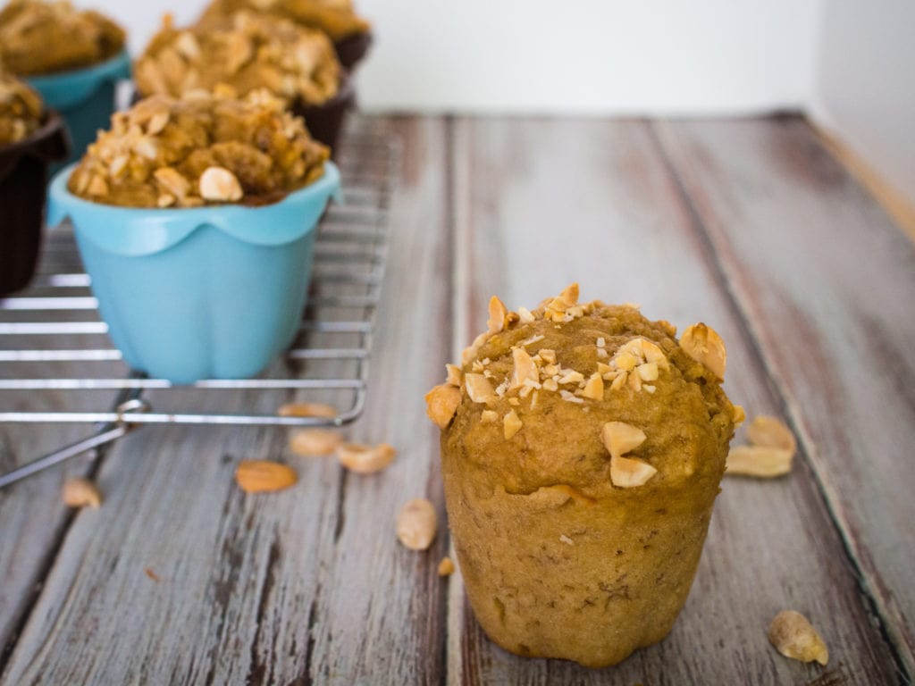 Peanut butter muffin surrounded by peanuts with more muffins on a cooling rack in the background.