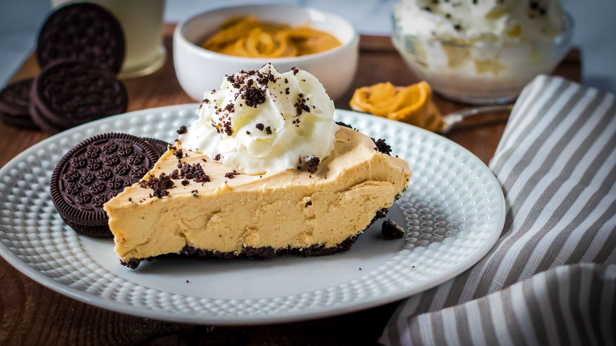 Side view of a slice of peanut butter pie topped with whipped cream on a plate.