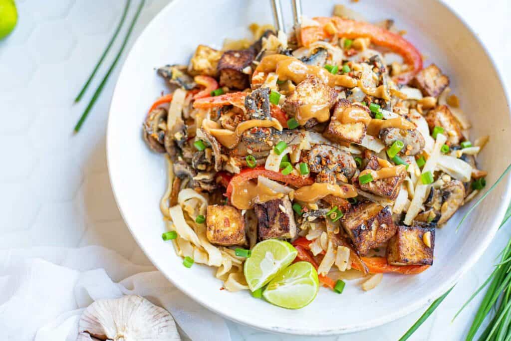 overhead shot of a bowl of noodles with vegetables and thai peanut sauce.