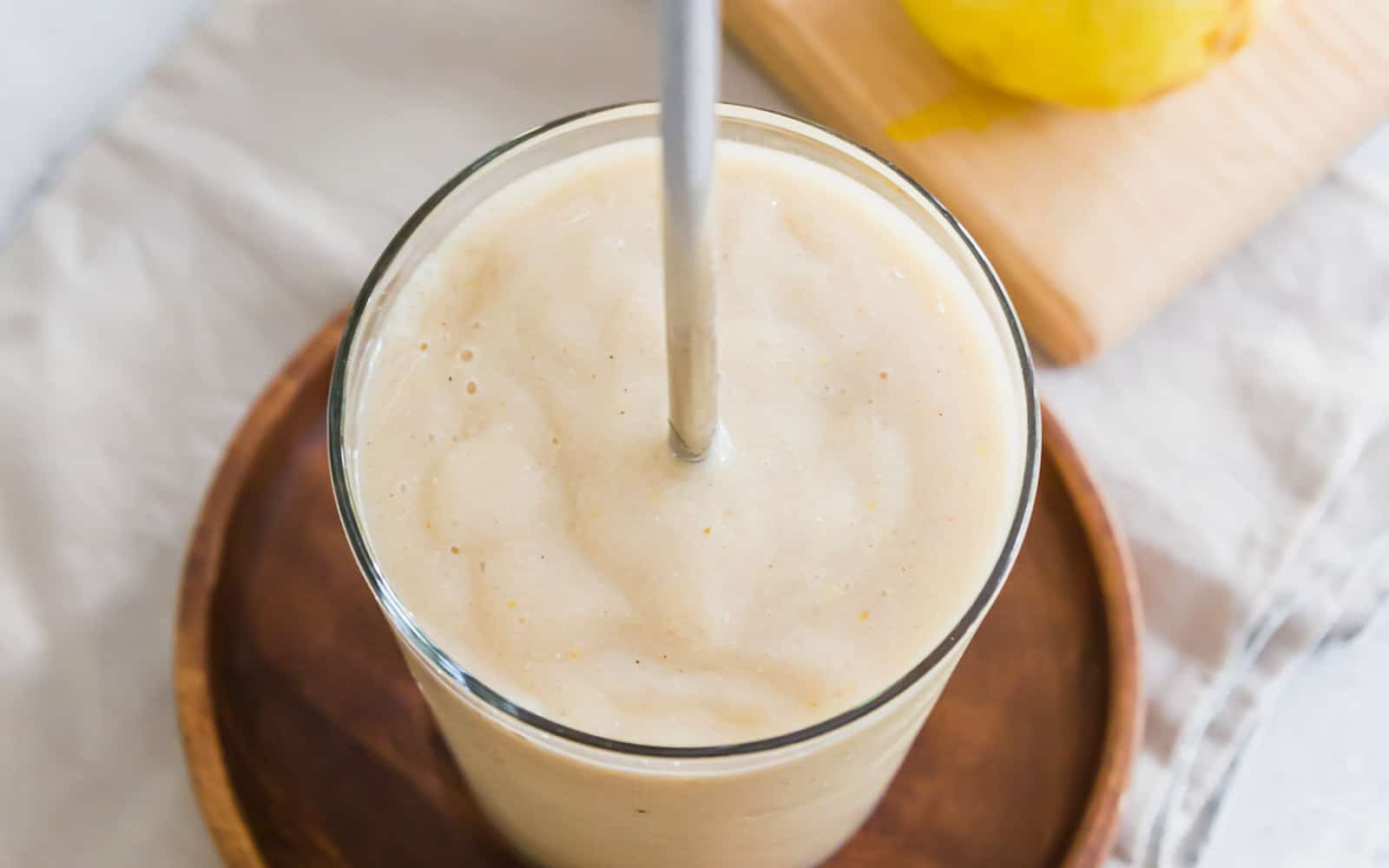 Pear smoothie in a glass with a metal straw.