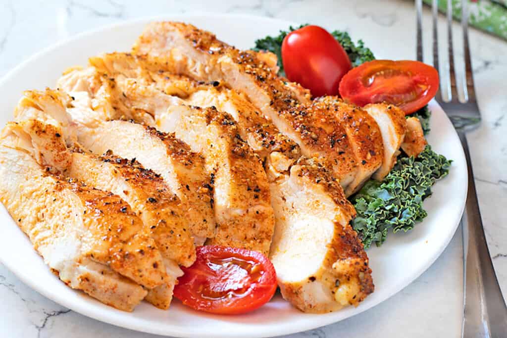 Perfect Baked Chicken Breasts on a white plate with vegetables.