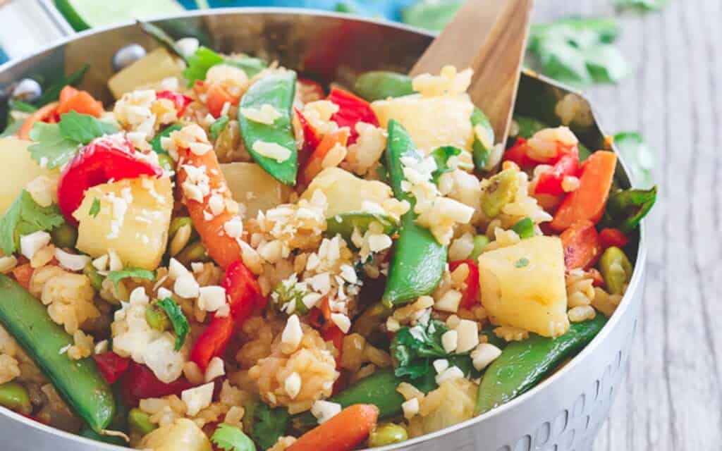 Pineapple fried rice with Thai vegetables in a metal bowl with wooden serving spatula.