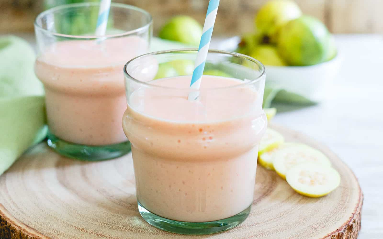 Guava pineapple smoothie in glasses with blue striped straw.