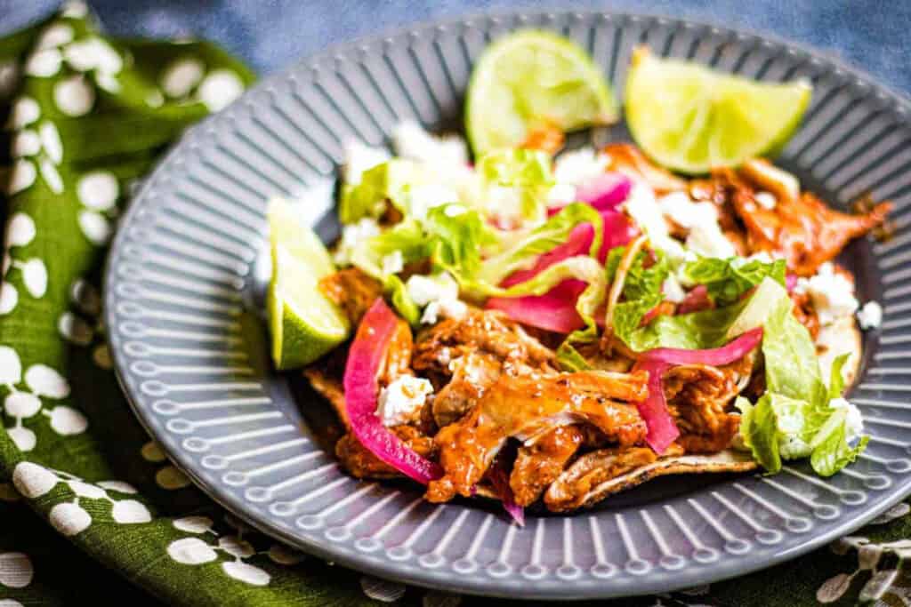 Pollo pibil on a grey plate with limes and shredded lettuce.