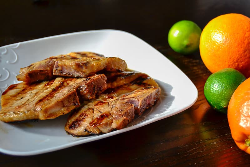 Grilled pork chops on a plate with oranges and limes.